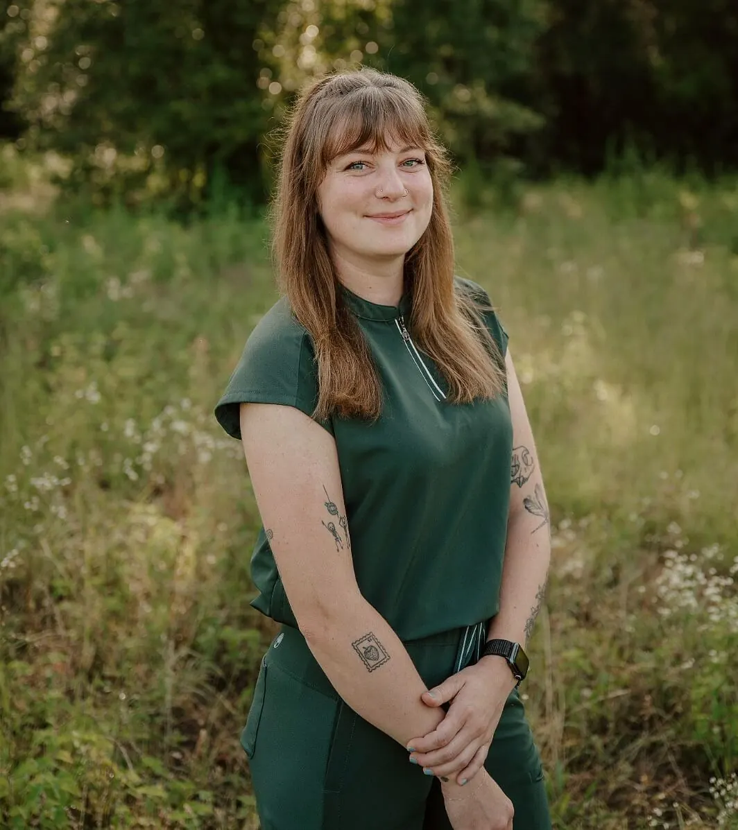Female wearing dark green scrubs with long brown hair