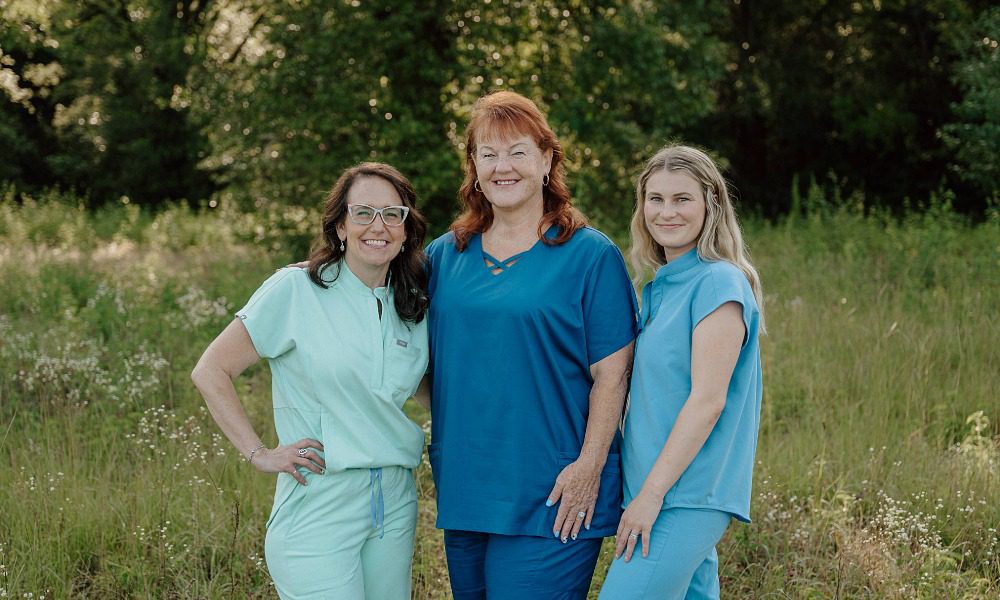 Group photo of 3 customer service representatives wearing different shades of blue scrubs