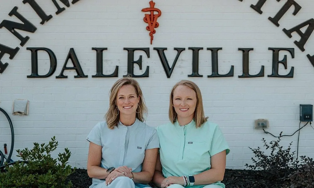 2 female veterinarians wearing lights shades of blue scrubs sitting on a bench